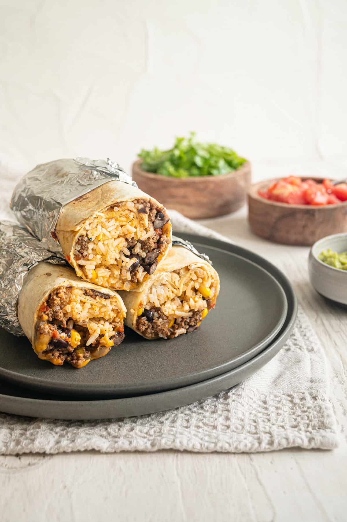 Three beef burrito halves wrapped in foil halfway stacked up on a plate.