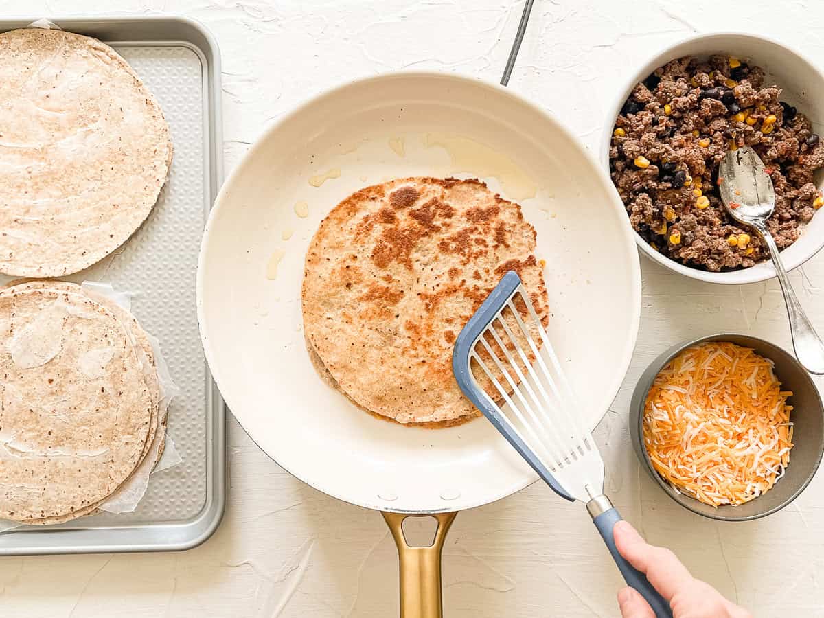 Quesadilla station with a skillet in the middle and a spatula finishing cooking a ground beef quesadilla.