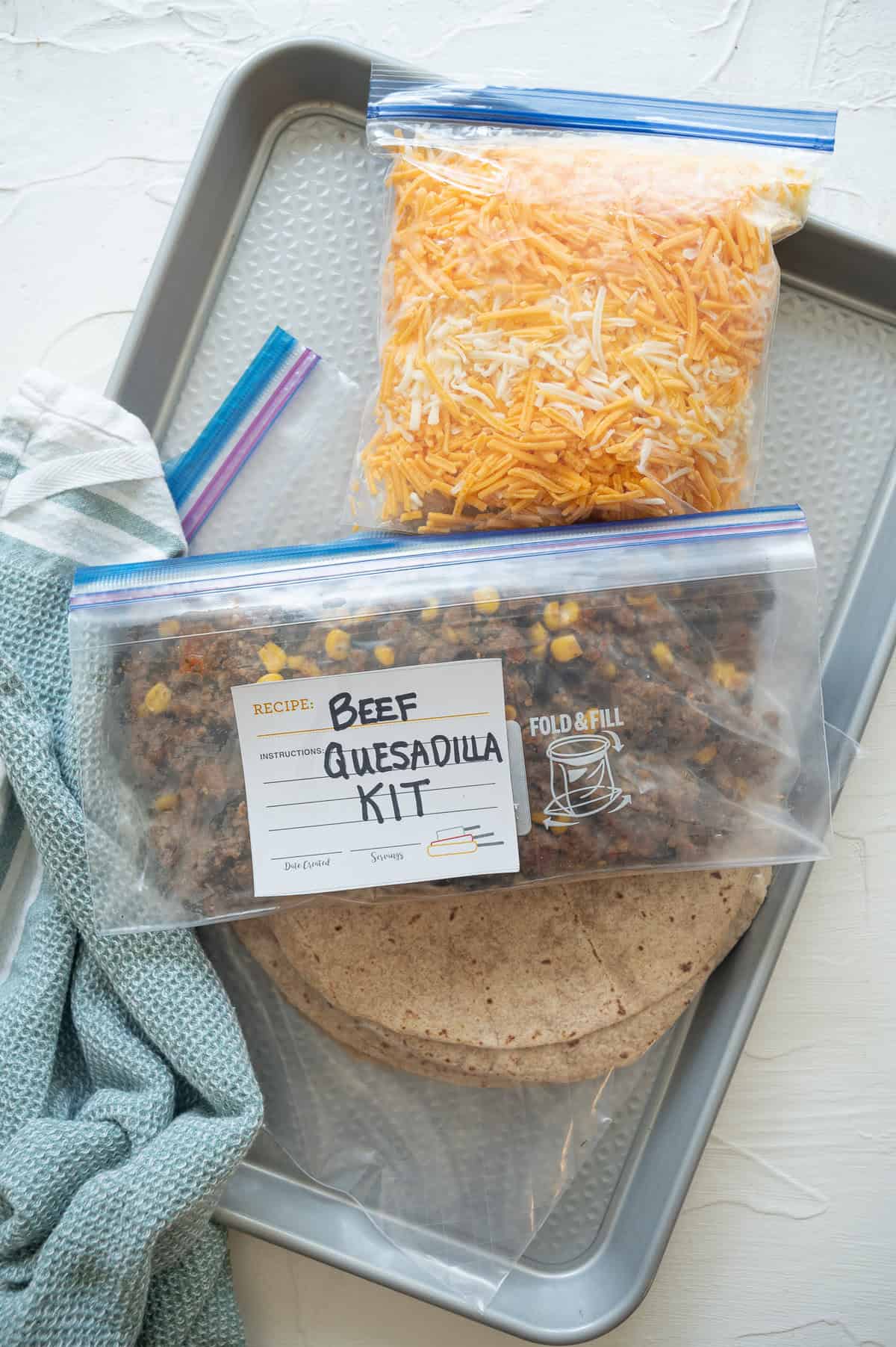 A freezer bag of tortillas, one with shredded cheese, and another one with ground beef mixture labeled Beef Quesadilla Kit.