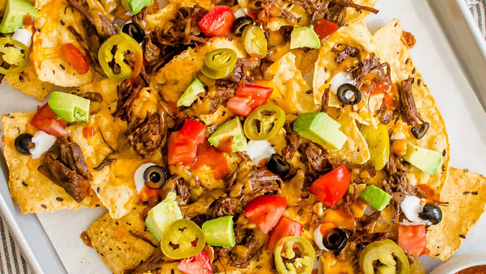 Shredded Beef Nachos on a pan with toppings ready to be served.