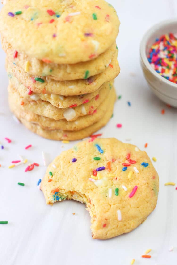 Seven funfetti cake mix cookies stacked up with one in front of the stack with a bite out of it.