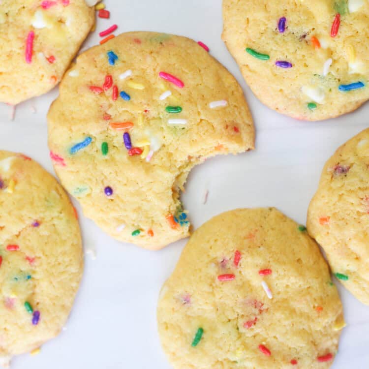 Funfetti cake mix cookies on parchment paper and one in the middle with a bite out of it.