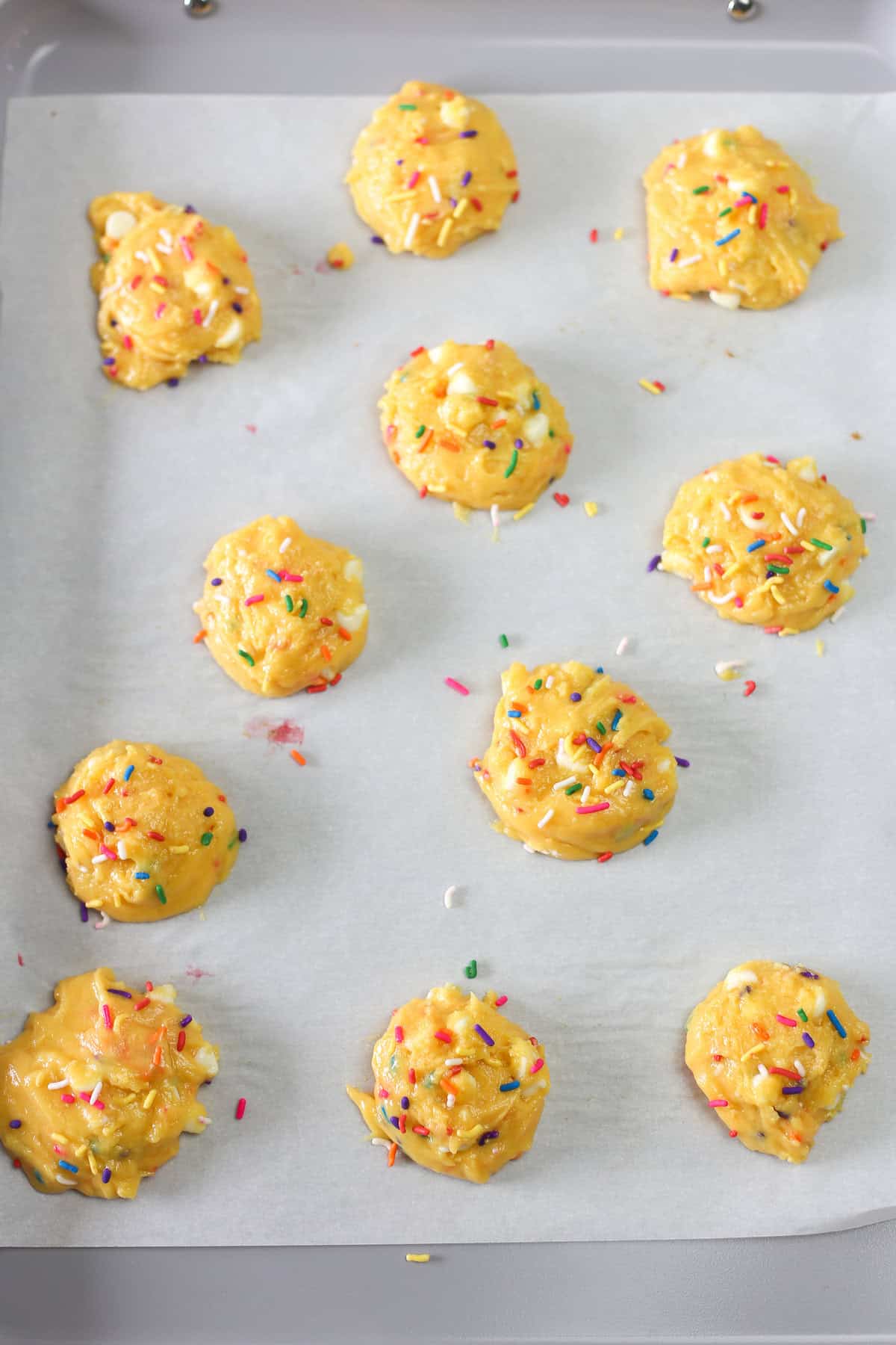 Funfetti cake mix cookie dough in balls on a parchment paper lined baking sheet ready for the oven.