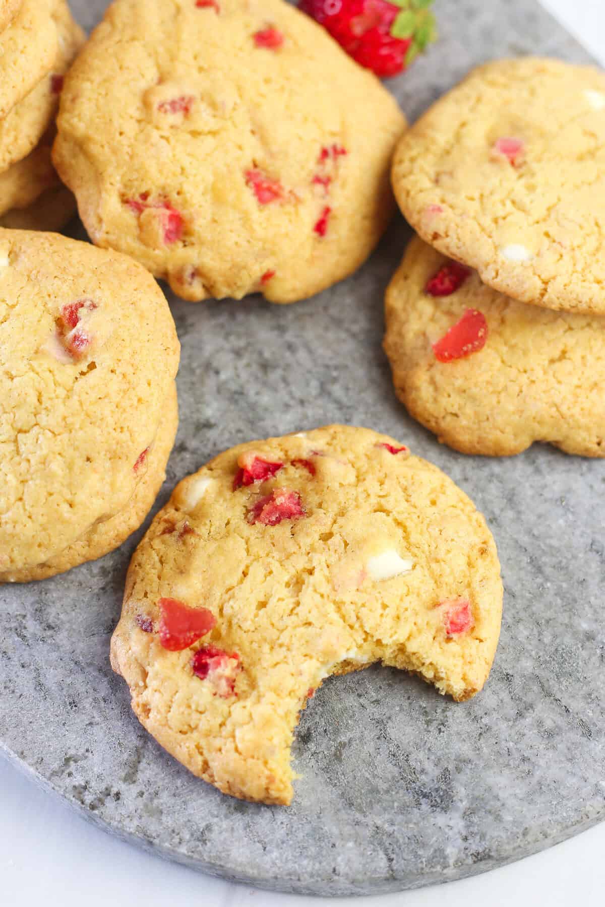 Strawberry cake mix cookies on a marble serving tray with a bite out of the cookie in front.