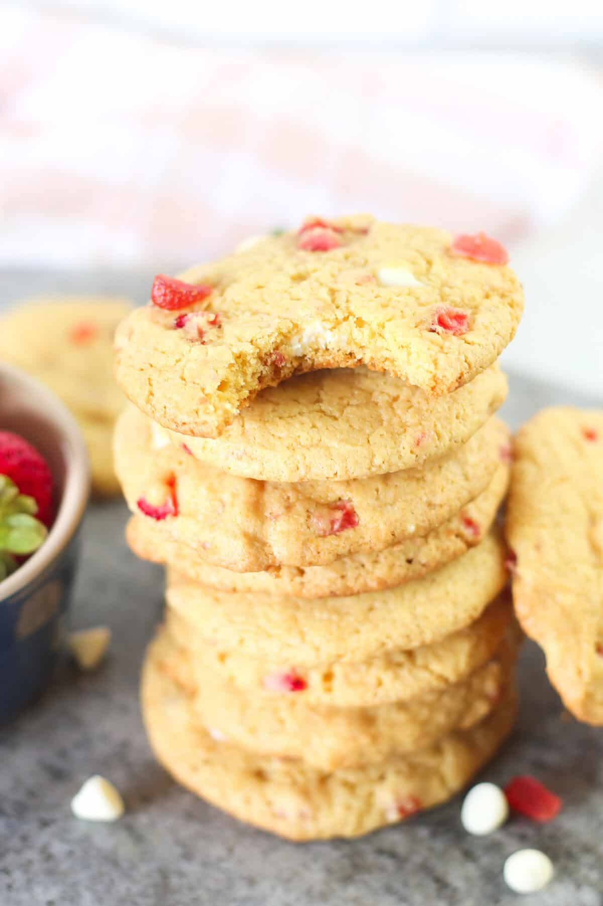 Eight strawberry cake mix cookies stacked on top of each other with a bite out of the very top one.