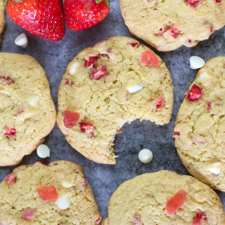 Strawberries and cream cake mix cookies lined up on a gray counter with white chocolate chips sprinkled around.