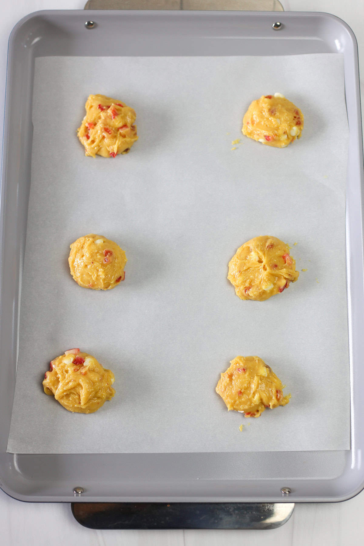 Strawberries and cream cake mix cookie dough in balls on a parchment lined baking sheet ready for the oven.