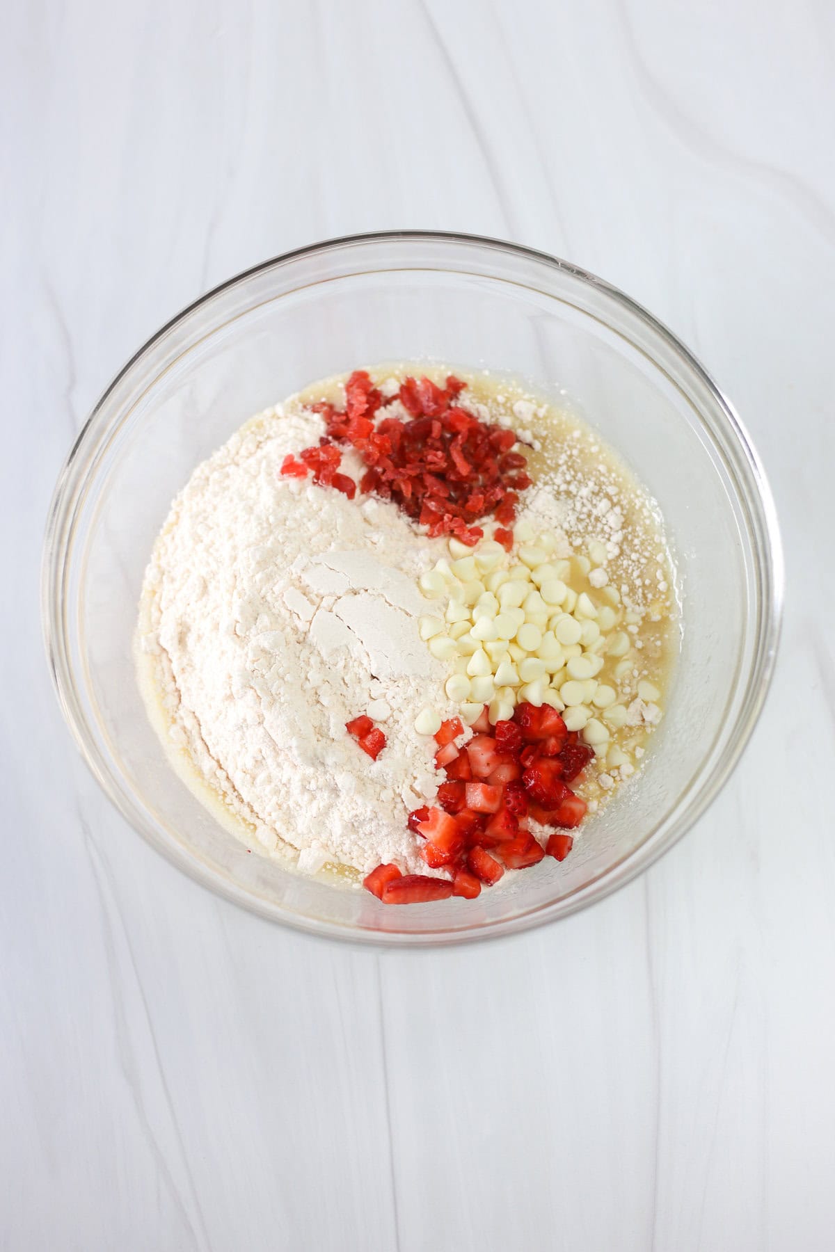 Cake mix, dehydrated strawberries, white chocolate chips, and diced strawberries being mixed into the wet ingredients of strawberries and cream cake mix cookies.