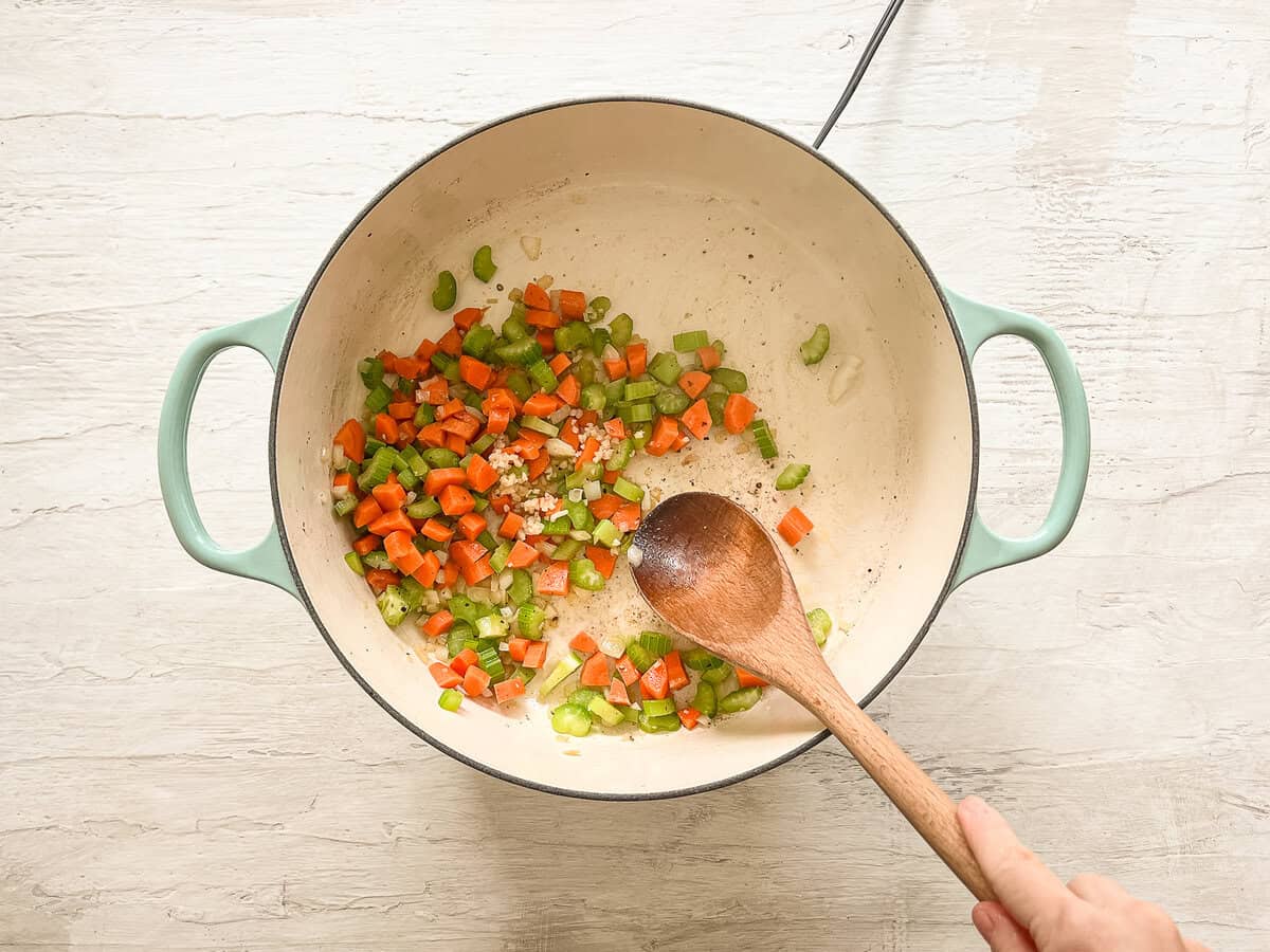 Minced garlic added to sauteed veggies in a ceramic pot.