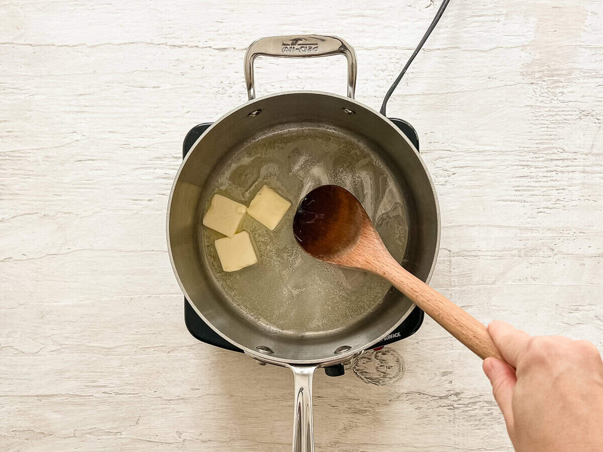 A wooden spoon stirring melted butter in a sauce pan.