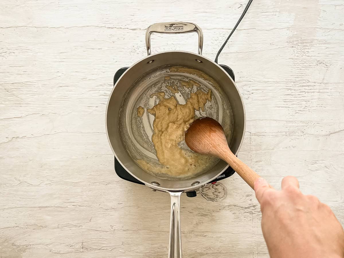 A wooden spoon stirring together flour and butter to make a roux.