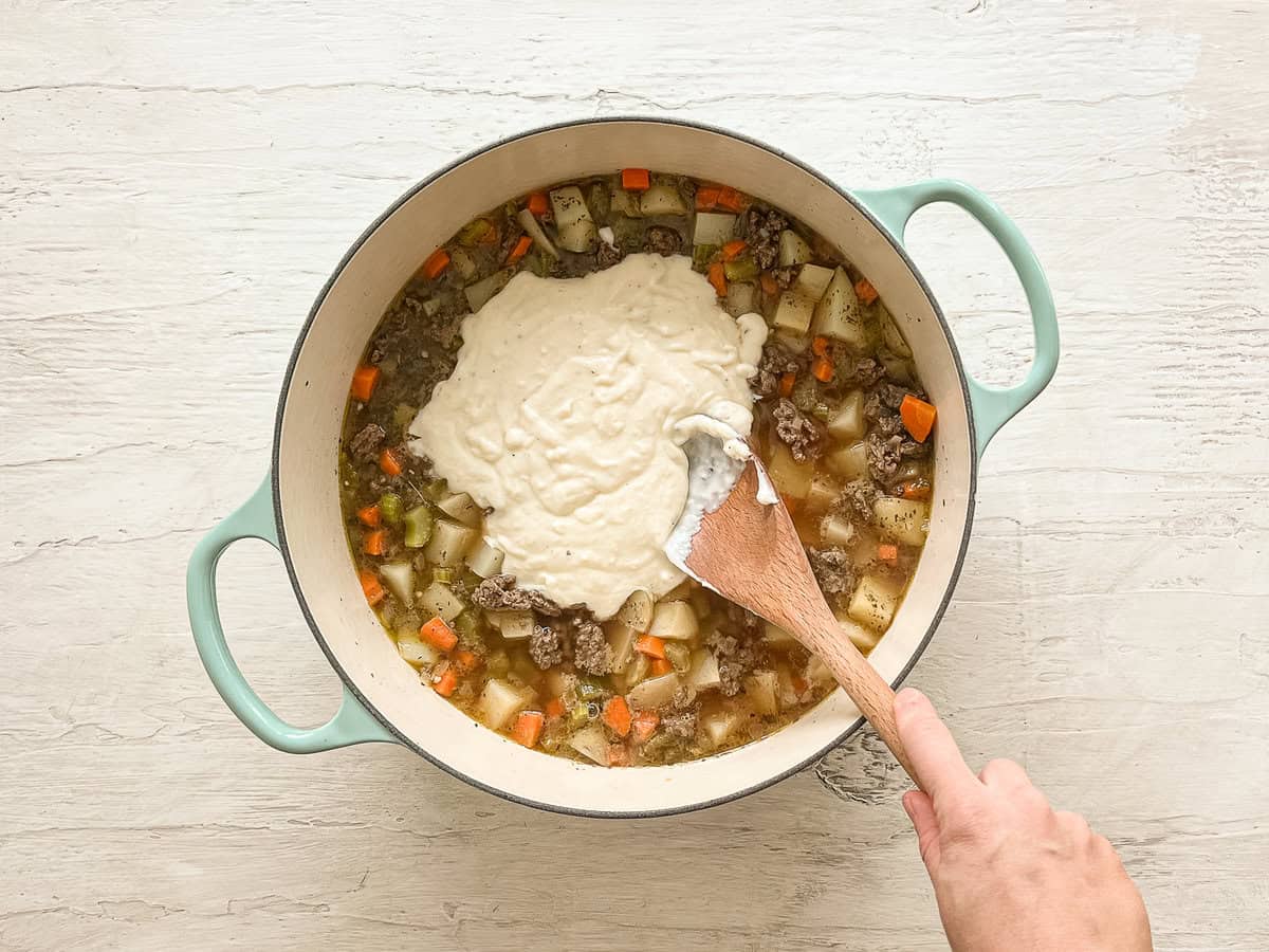 A roux being mixed into a pot with other ingredients for cheeseburger soup.