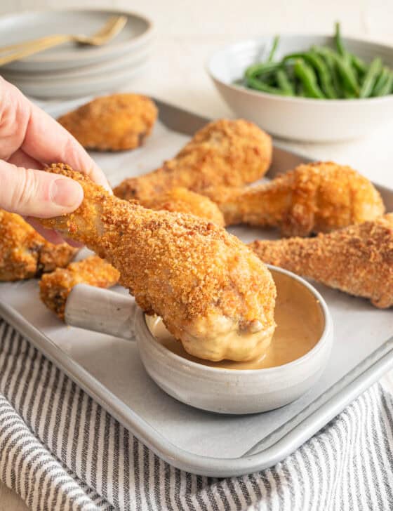 A crispy baked drumstick being dipped in a bowl of honey mustard sauce.