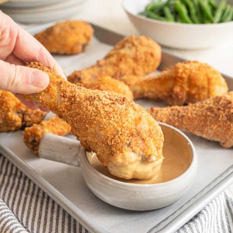 A crispy baked drumstick being dipped in a bowl of honey mustard sauce.