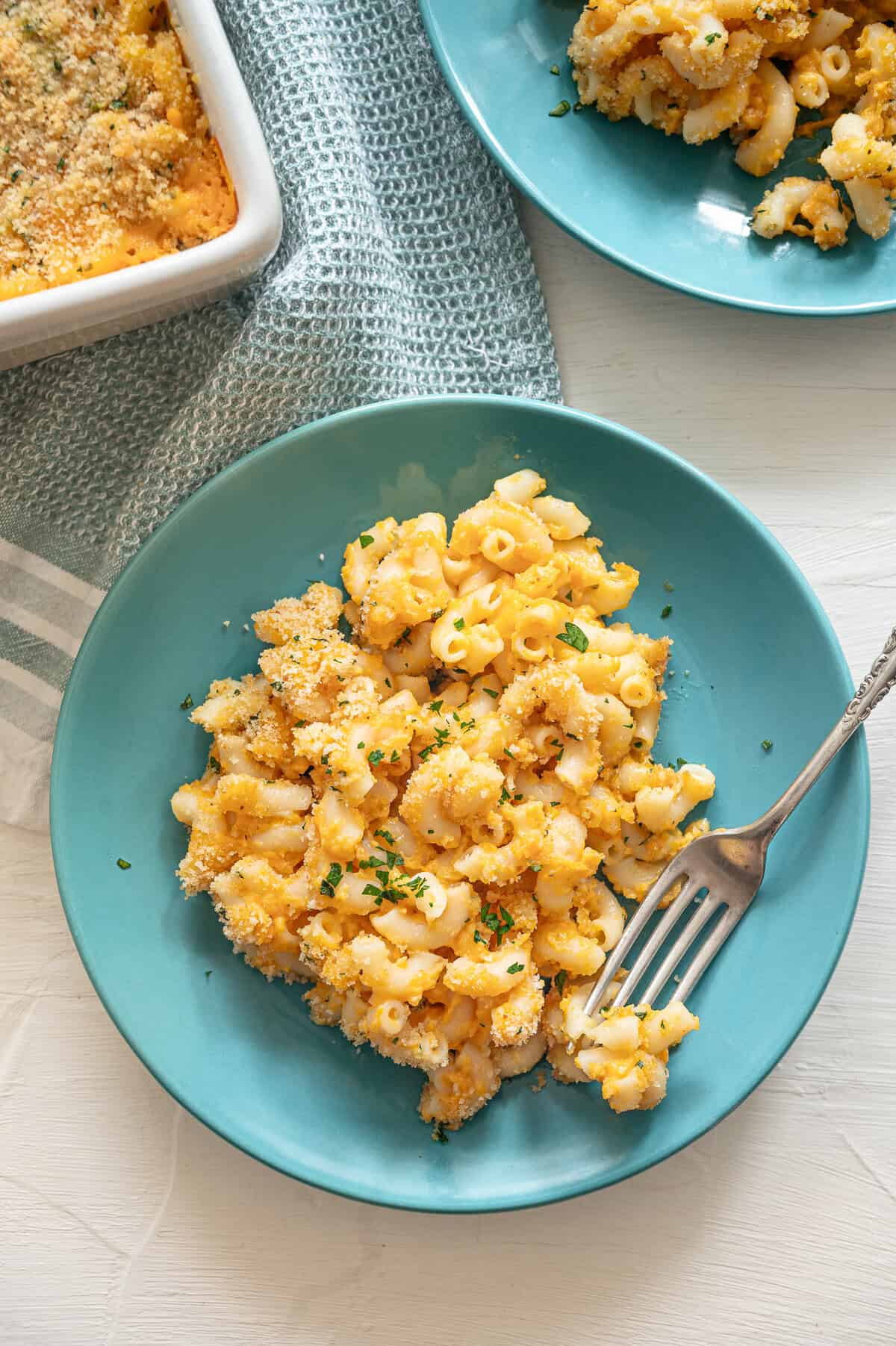 A serving of healthy mac and cheese on a teal plate with a fork.