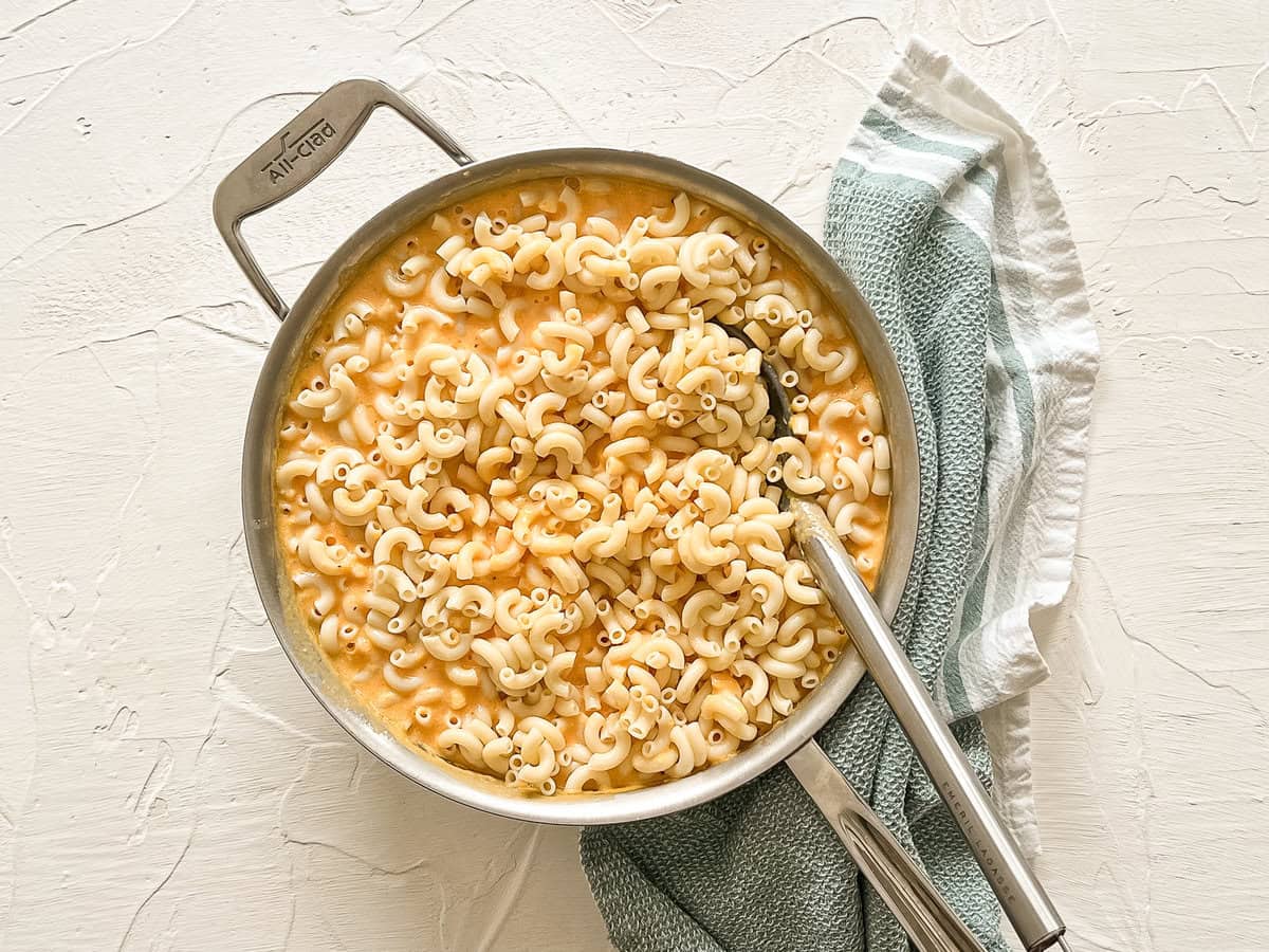 Cooked elbow noodles being stirred into homemade cheese sauce in a pan.