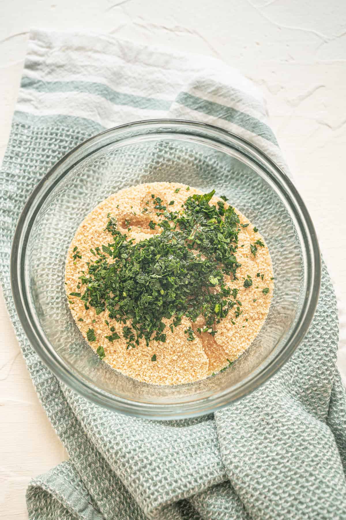 A mixing bowl with breadcrumbs, oil, and parsley being mixed together to put on top of macaroni and cheese.