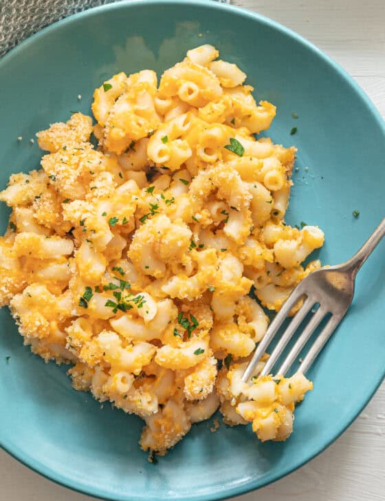 A teal plate with a serving of baked mac and cheese and a fork on it.