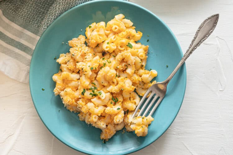 A teal plate with a serving of baked mac and cheese and a fork on it.