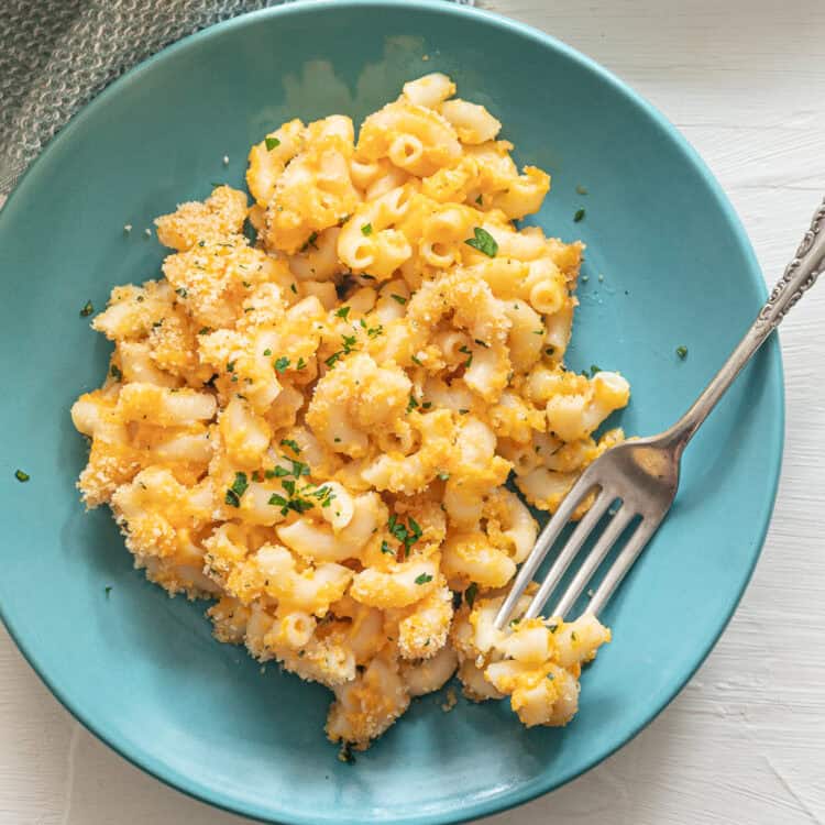 A teal plate with a serving of baked mac and cheese and a fork on it.