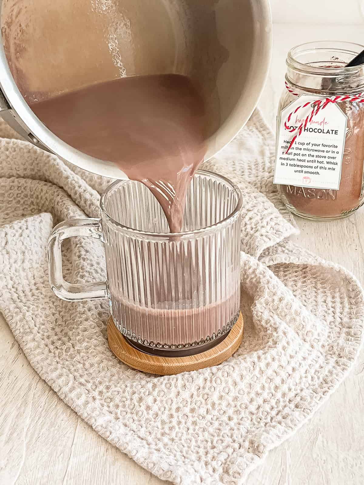 Homemade hot chocolate being poured from a sauce pan into a glass mug.