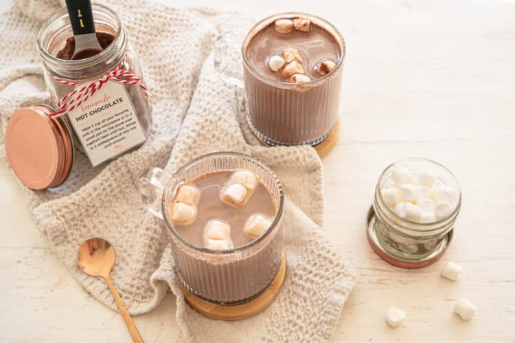 Homemade hot chocolate mix in a mason jar with two mugs of hot chocolate and mini marshmallows ready to drink.