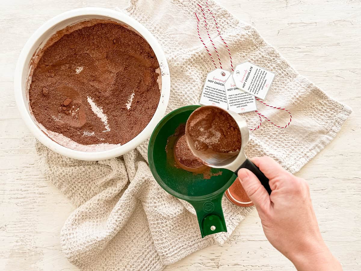 Homemade hot chocolate mix being poured through a funnel into a mason jar.