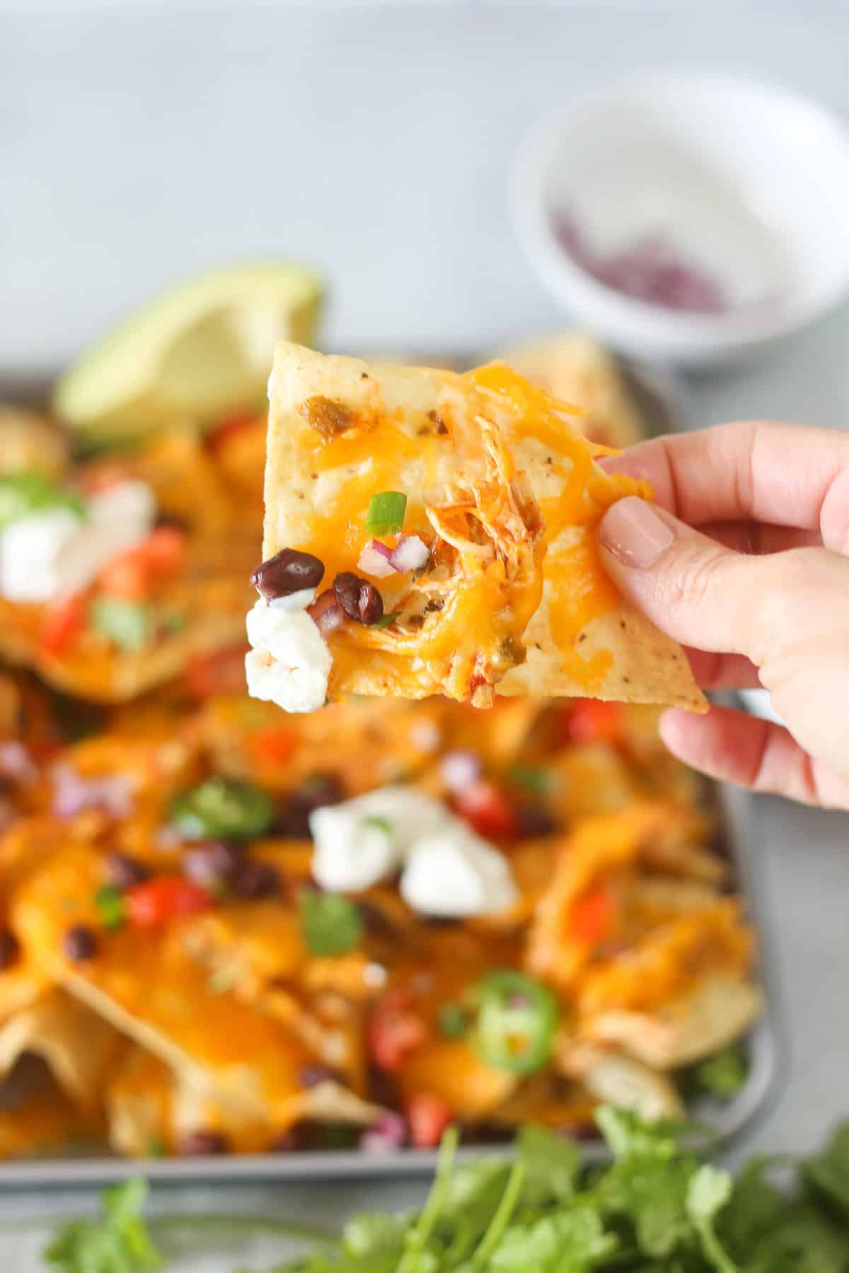 A hand holding a nacho with toppings on it. 