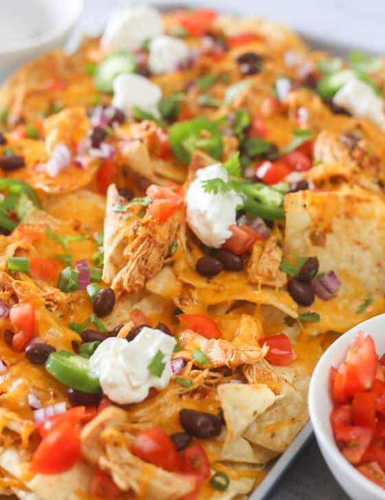 A sheet pan full of shredded chicken nachos with toppings.