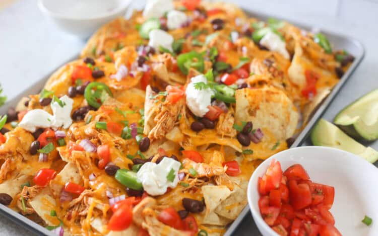 A sheet pan full of shredded chicken nachos with toppings.