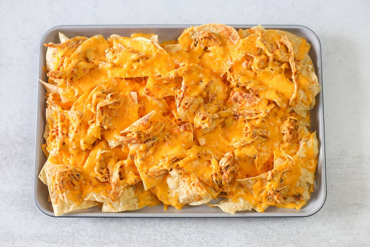 Tortilla chips with melted shredded cheese on top of them on a baking sheet. 