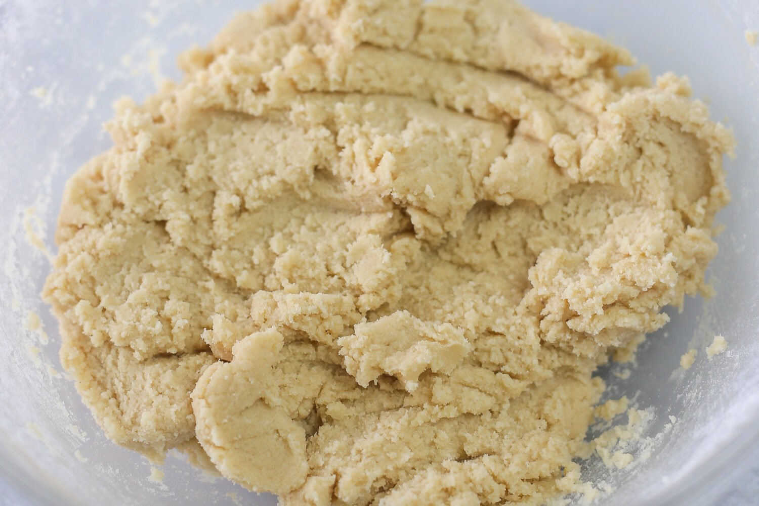 Snickerdoodle cookie dough all mixed up in a glass bowl ready to be made into balls and rolled in cinnamon/sugar.