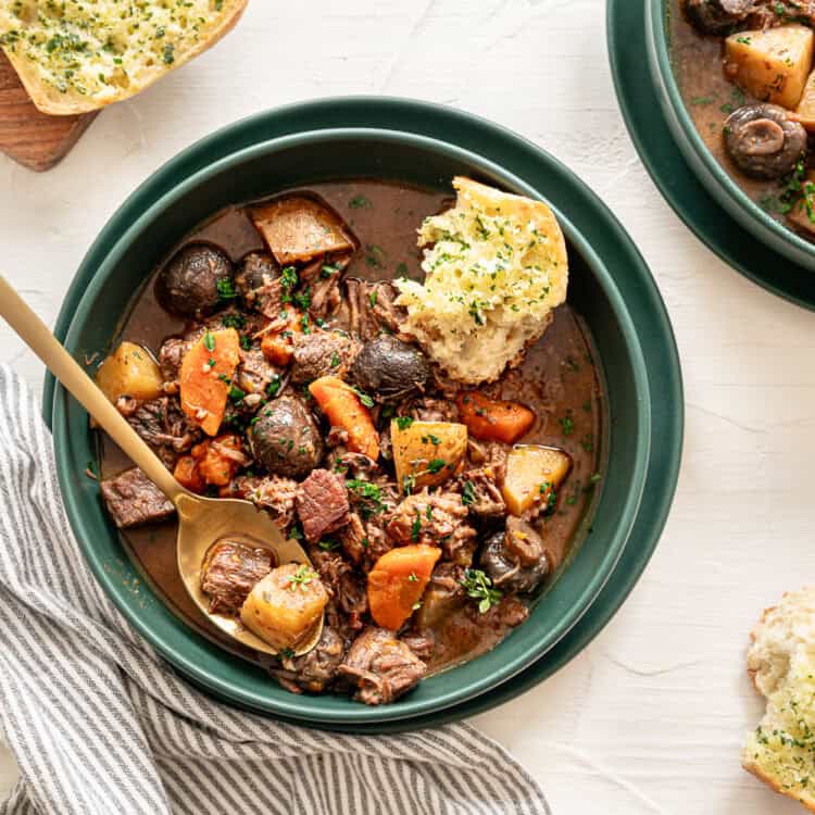 A bowl of beef bourguignon with crusty bread on the side.