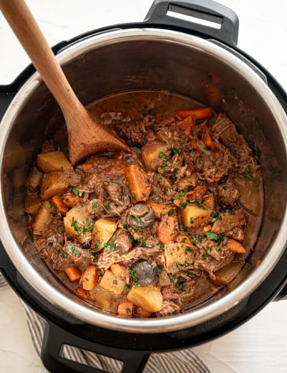 Beef bourguignon in an Instant Pot with a wooden spoon scooping up a serving.