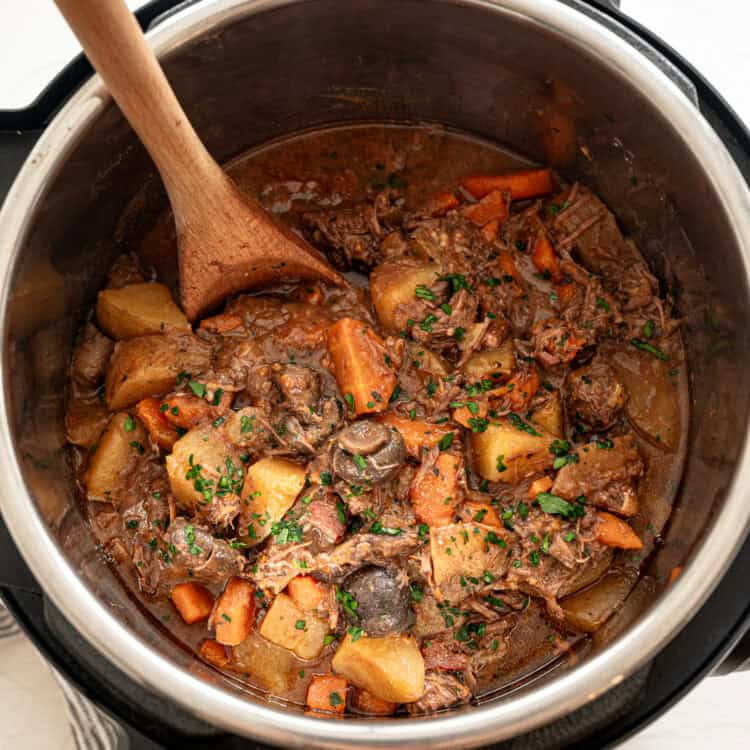 Beef bourguignon in an Instant Pot with a wooden spoon scooping up a serving.