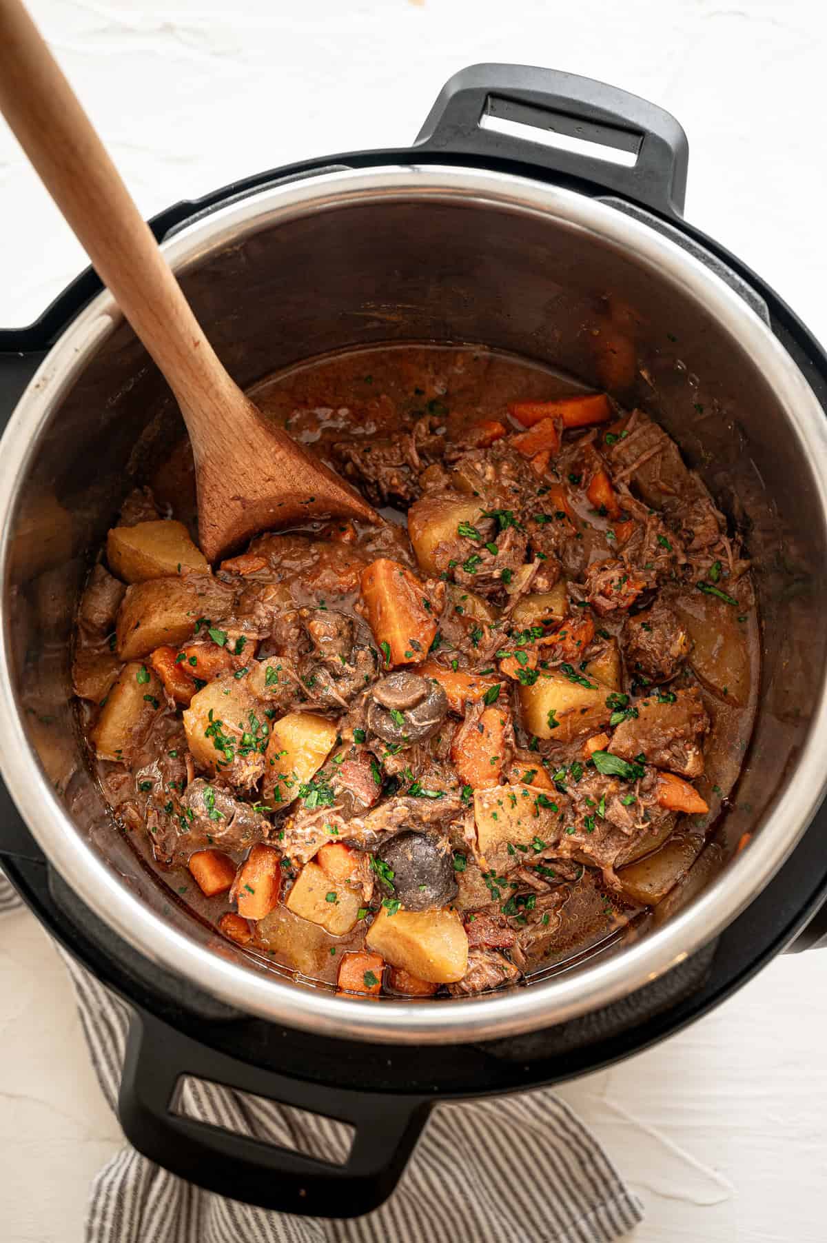 Beef bourguignon in an Instant Pot with a wooden spoon scooping up a serving.