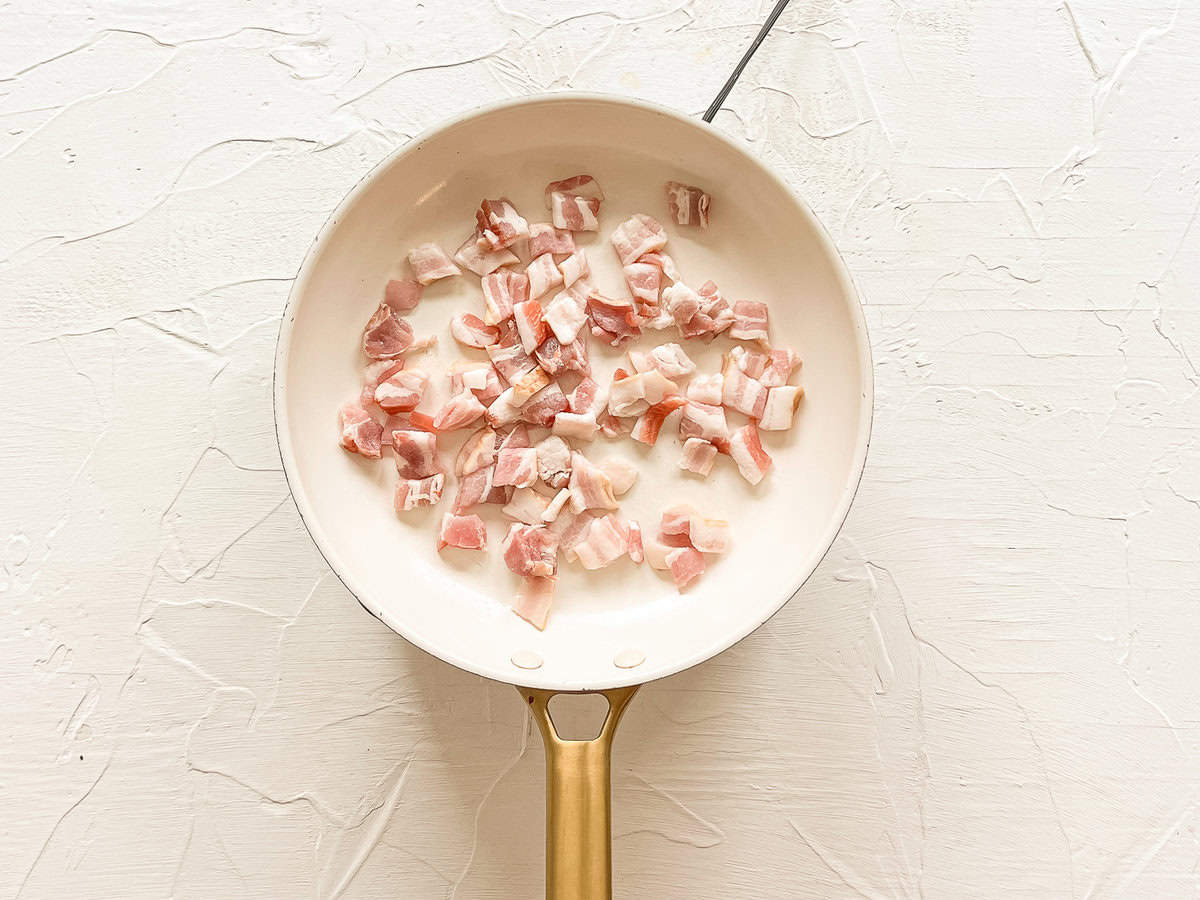 Chopped up bacon sauteeing in a skillet.