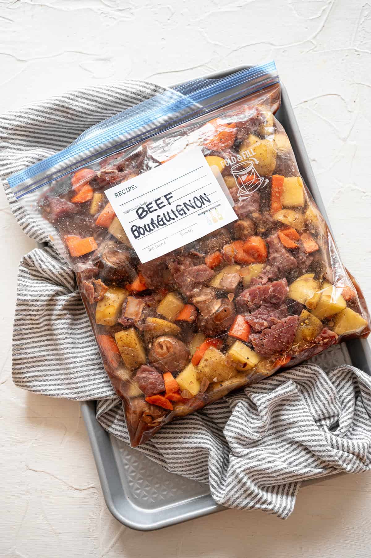 Raw ingredients for beef bourguignon in a freezer-safe gallon-size bag ready to freeze.