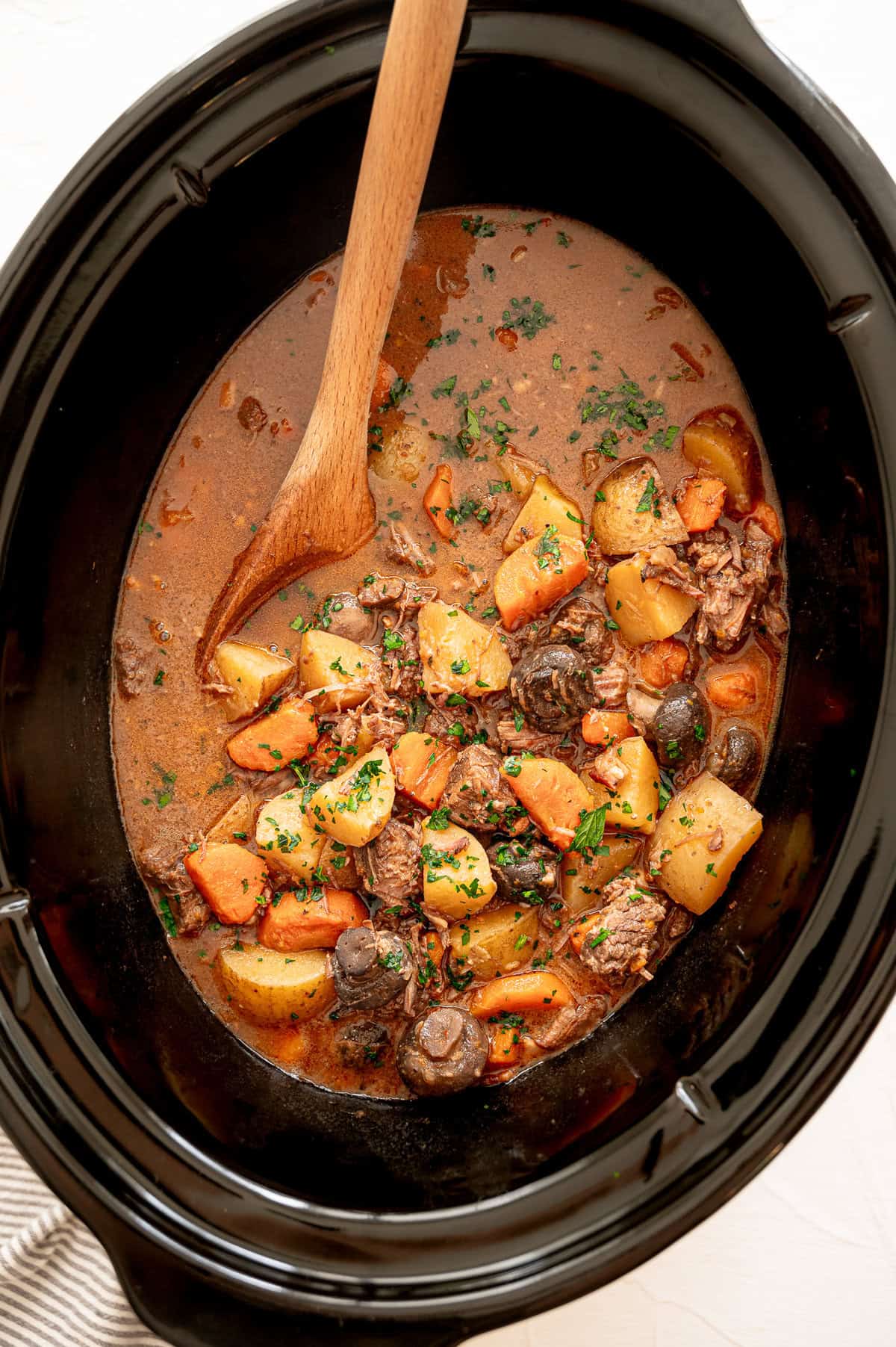 Beef bourguignon in a crock pot ready to serve with a wooden spoon.