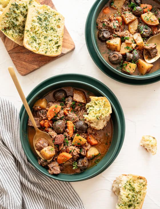 Two bowls of beef bourguignon with texas toast slices on a cutting board.