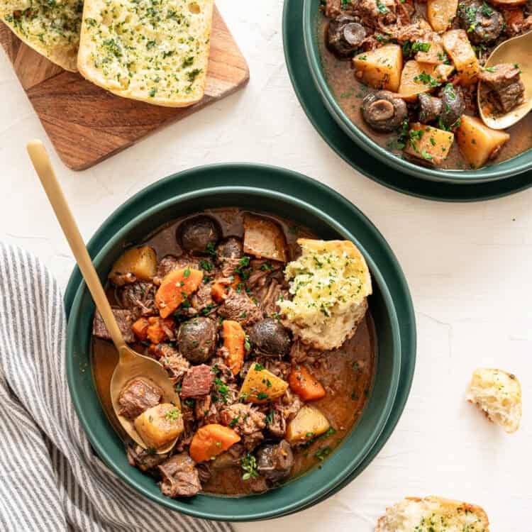 Two bowls of beef bourguignon with texas toast slices on a cutting board.