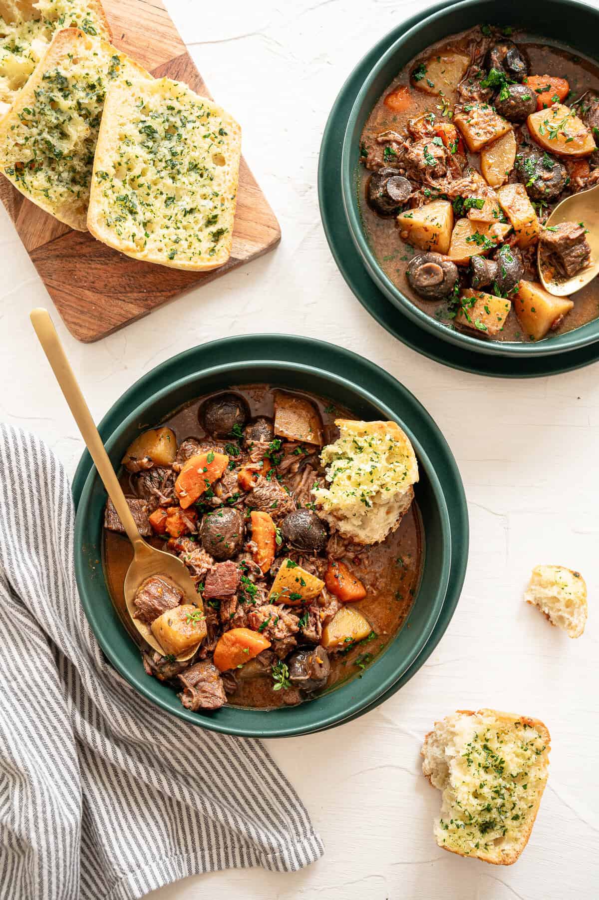 Two bowls of beef bourguignon with texas toast slices on a cutting board.