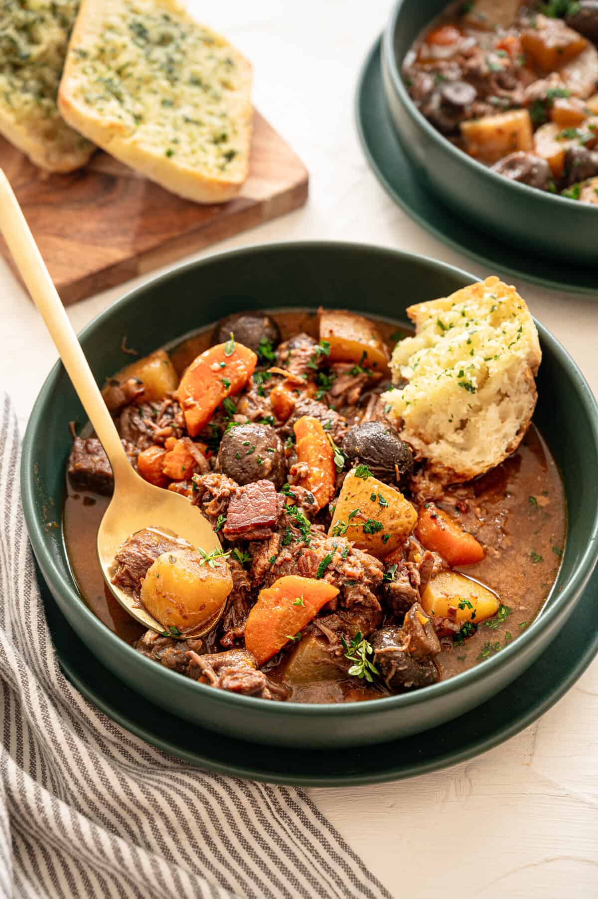 Beef bourguignon in a bowl with a spoon and a piece of crusty bread in it.