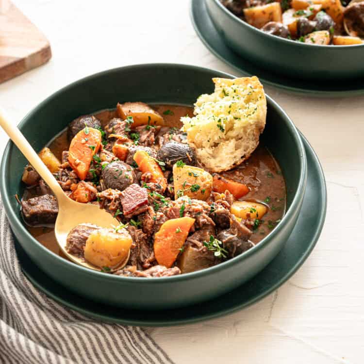 A bowl of beef bourguignon with a piece of crusty bread in the bowl.