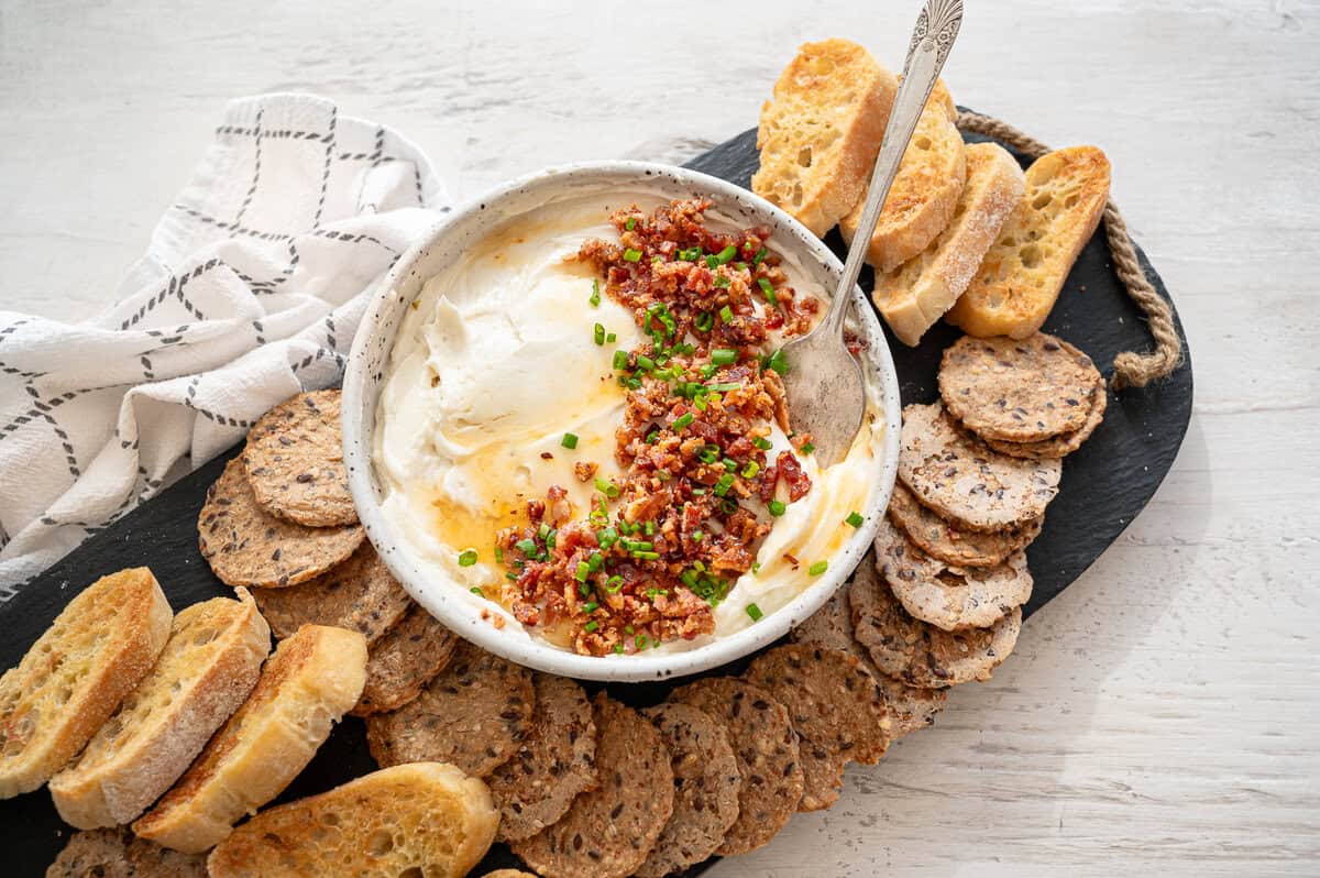 Honey whipped goat cheese with chopped bacon and chives on a tray of crackers.