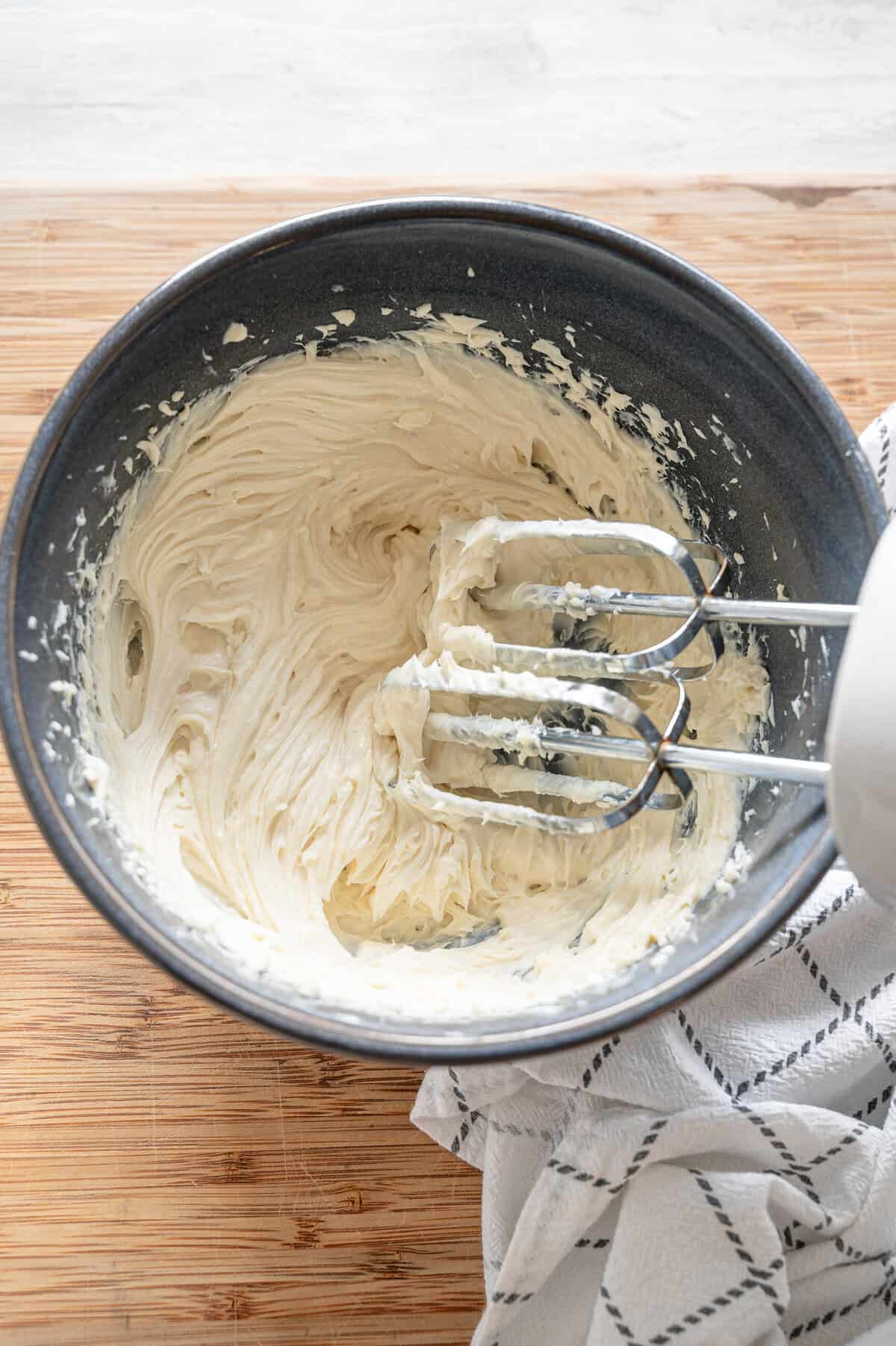 A hand mixer whipping cream cheese, goat cheese, and honey together in a bowl.