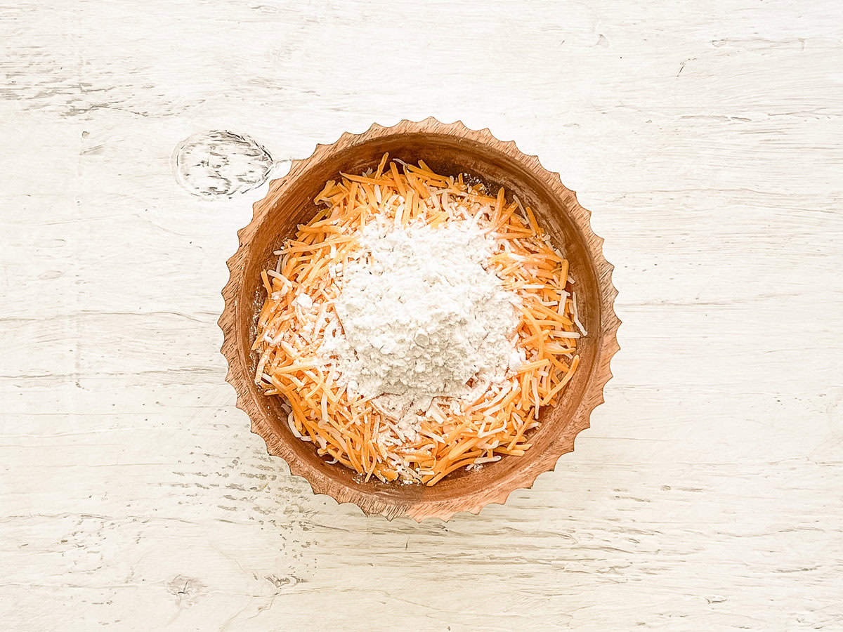 A bowl of shredded cheddar cheese with flour on top of it.