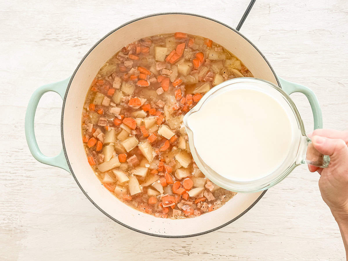 Milk being poured into a pot with ingredients for autumn chowder.