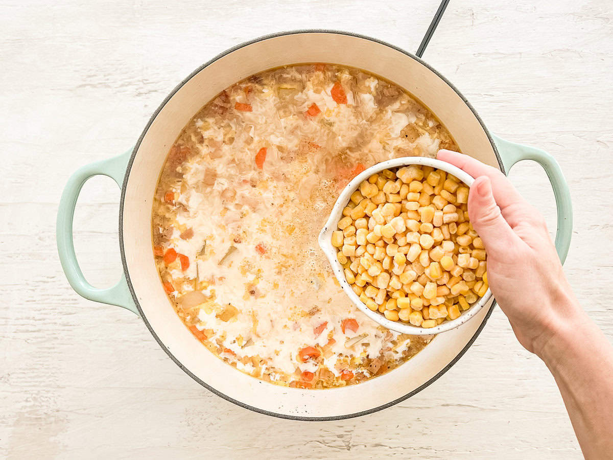 Frozen corn being dumped into a pot with autumn chowder ingredients ready to cook.