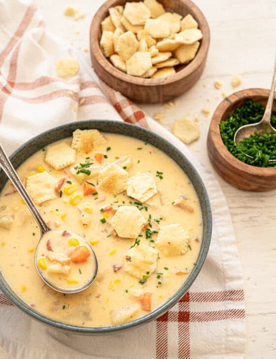 Potato corn chowder in a gray bowl with oyster crackers and chopped chives on top.